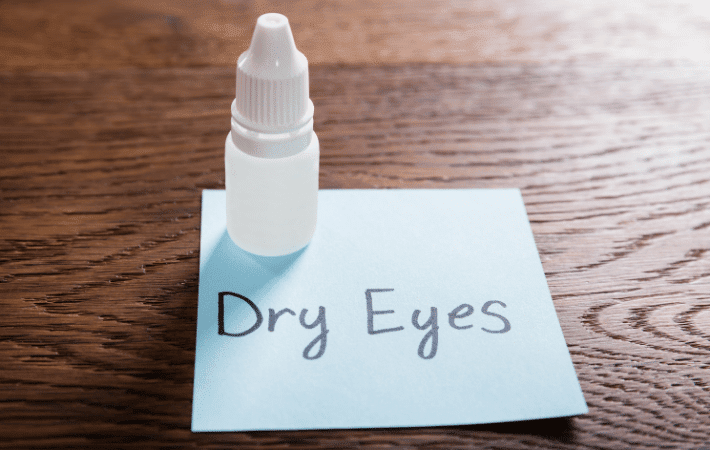 "Dry eye" written on sticky note on desk with eye drops on top