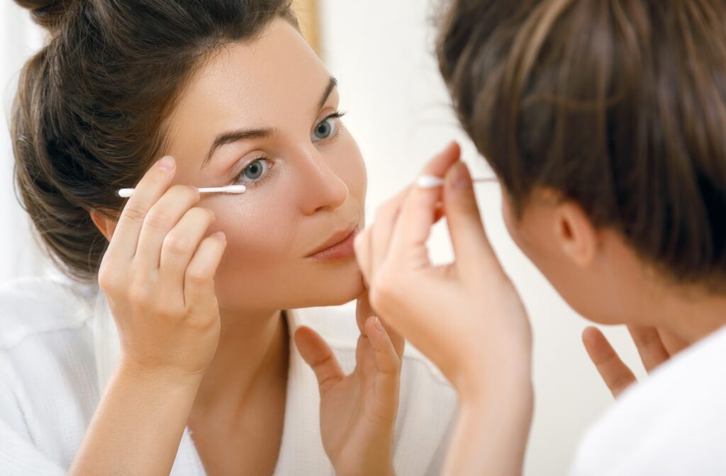 Young woman in front of mirror using a swab to cleans her eyelids