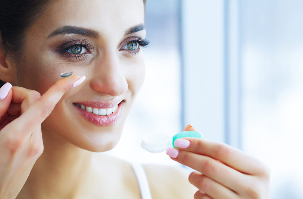 Women putting in contact lenses in her eyes while holding contact lens case in other hand