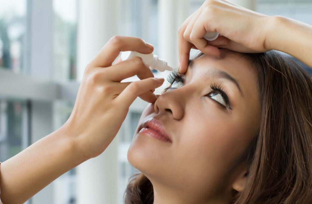 A woman in the process of lubricating her dry eyes with artificial tears.