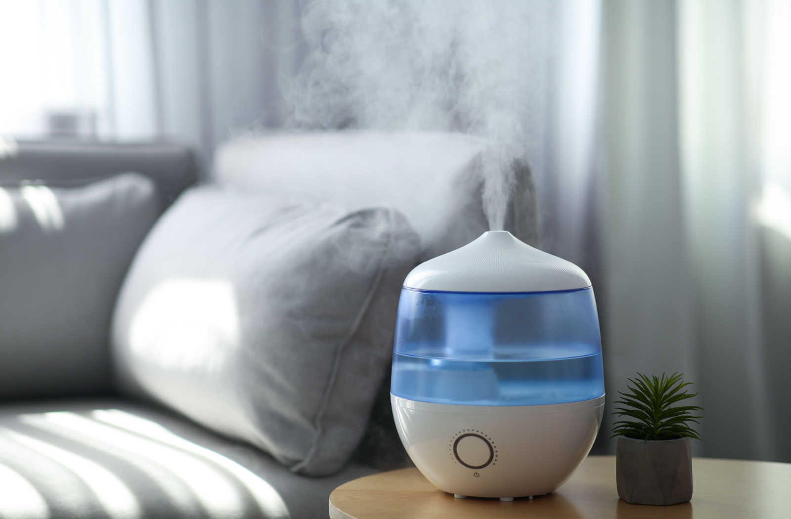 A humidifier placed on a table with a grey couch in the background to help reduce dryness in the atmosphere that can lead to dry eye.