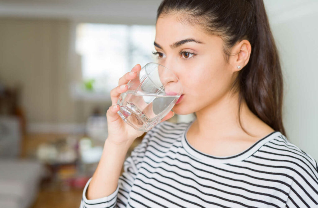 A young woman wearing a striped t-shirt, hydrating herself by drinking water from a glass.