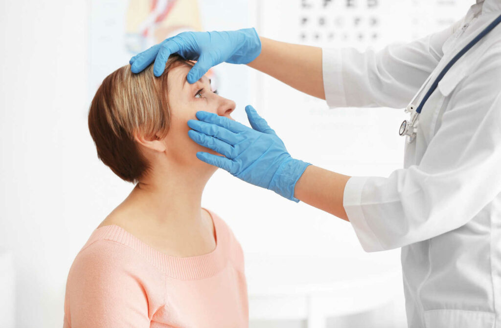 An optometrist checking a female patient's eye wearing blue gloves and a doctor's white coat.