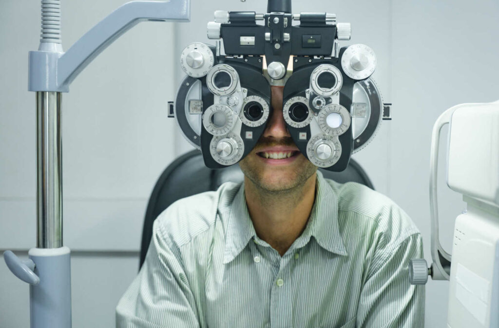 A man sitting in an optometrist's office and smiling while looking into a machine that tests his vision.