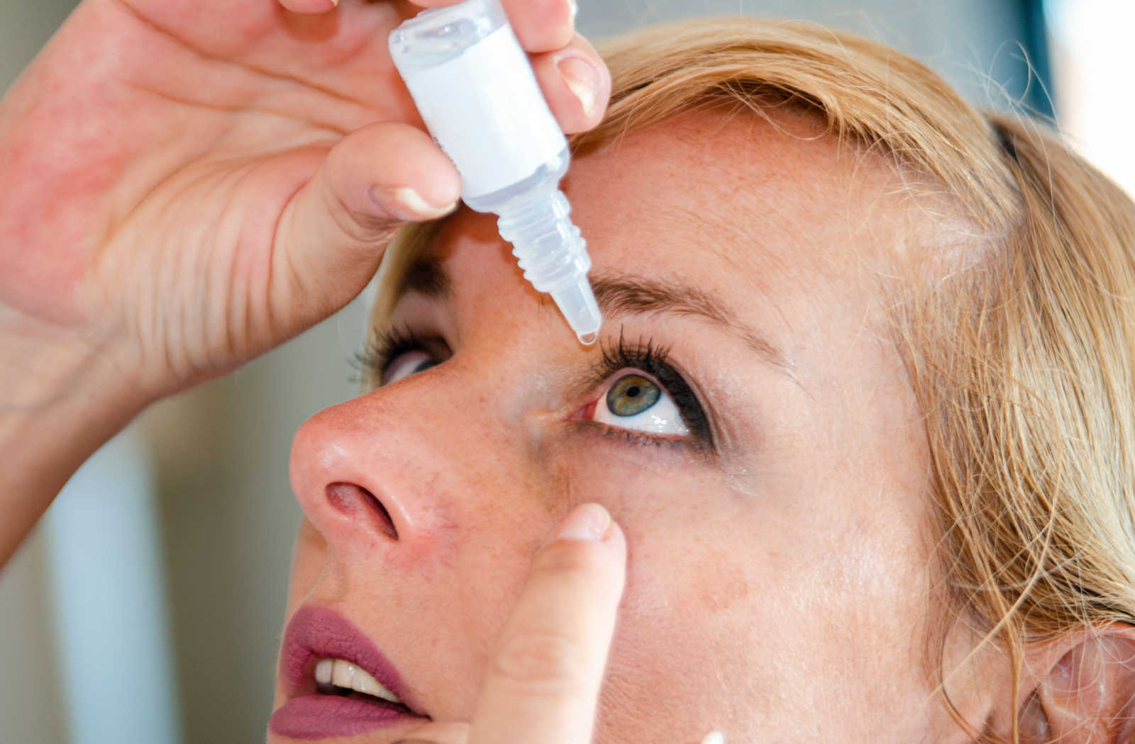 A close-up of a woman applying eye drops in her eye.