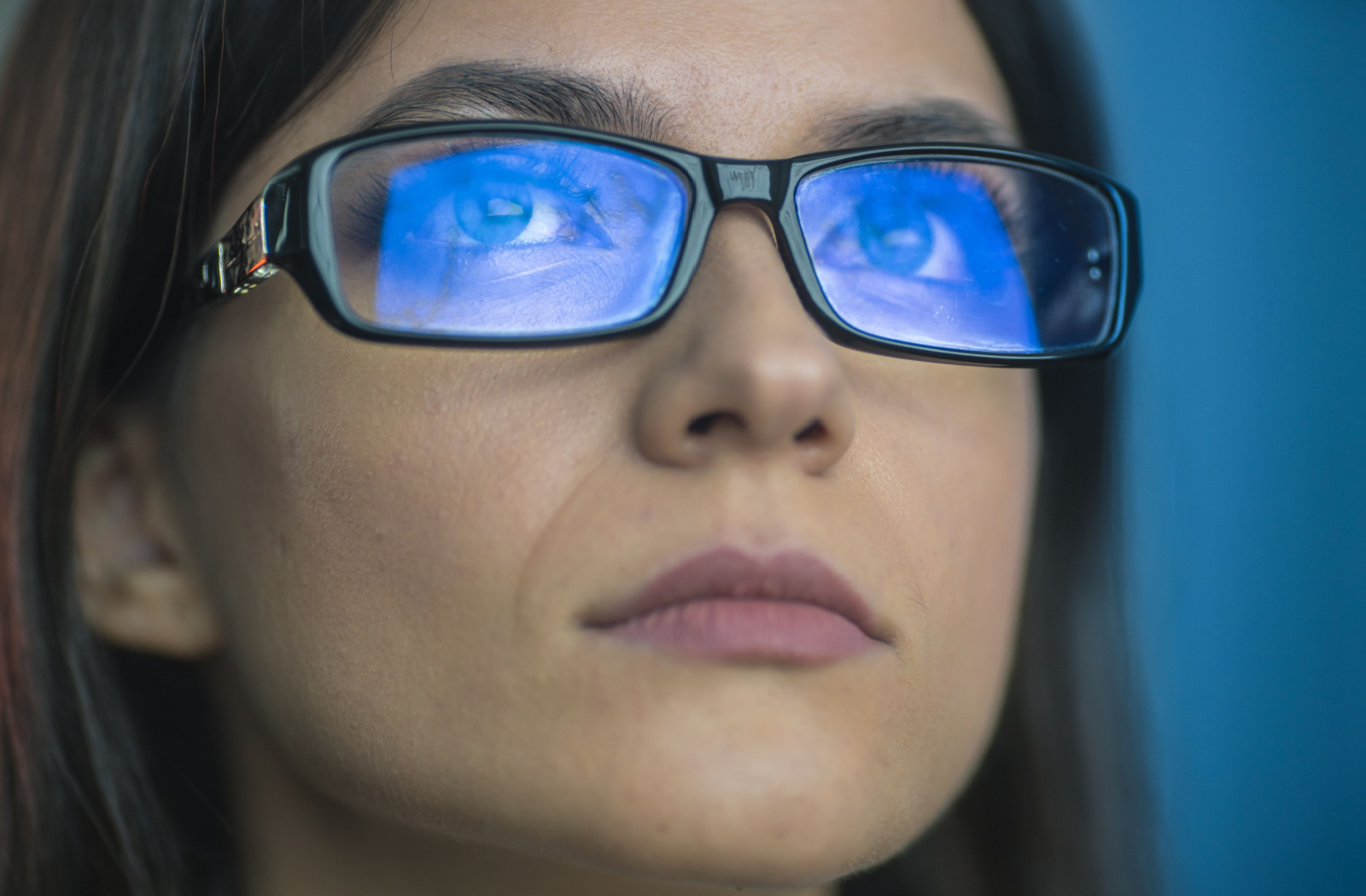 A woman with blue light reflected on her glasses from a screen.
