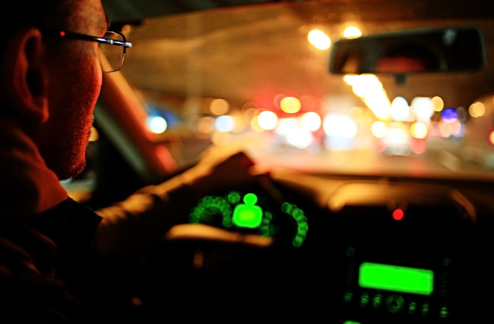 A man driving his car at night wearing a pair of eyeglasses.