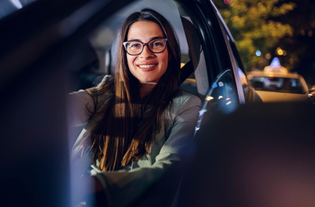 A beautiful woman seated in the driver's seat wearing glasses and looking into the camera