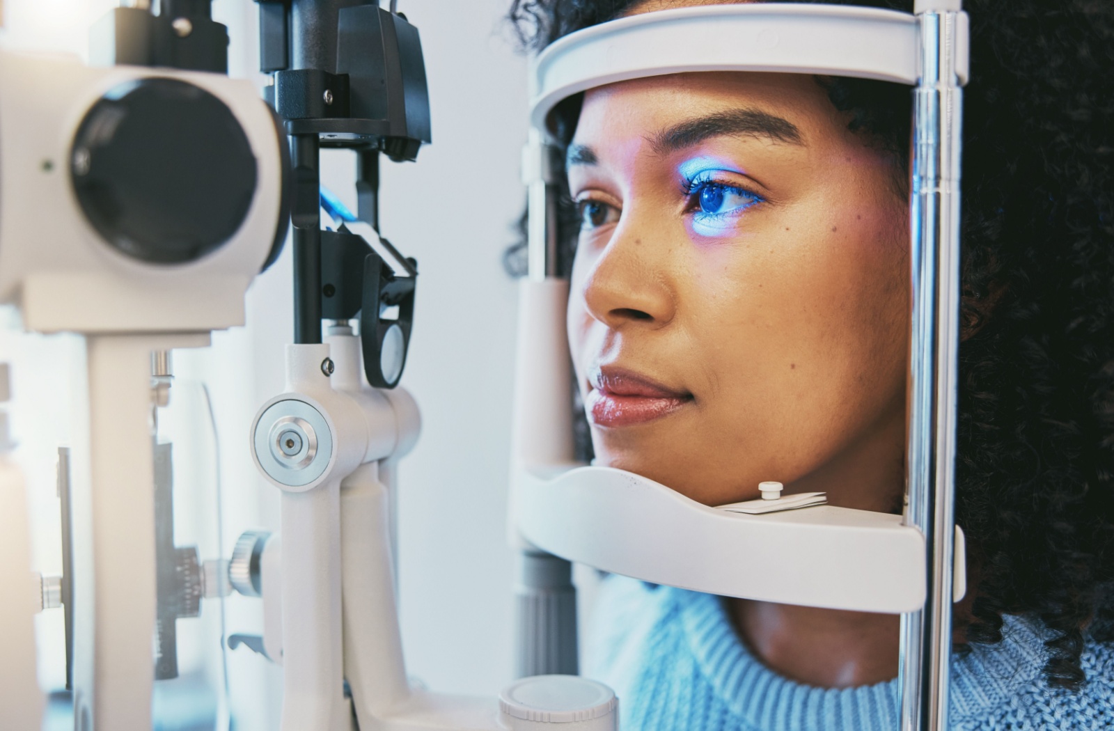 A patient in a blue sweater sitting with her chin and forehead against the rests for a slit lamp exam during her regular eye exam.