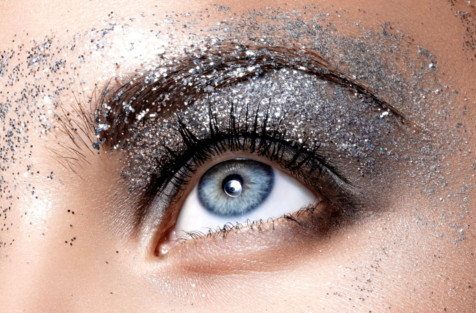 A bright blue eye decorated with mascara, dark eyeshadow, and silver glitter