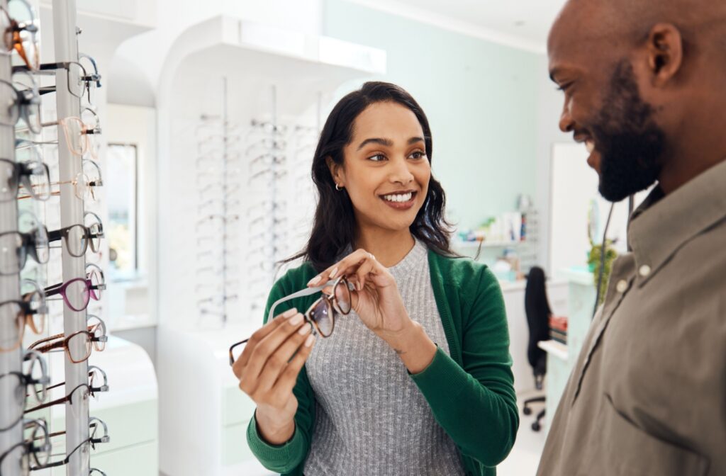 A person shopping for glasses and smiling as they show their friend a pair they're considering.