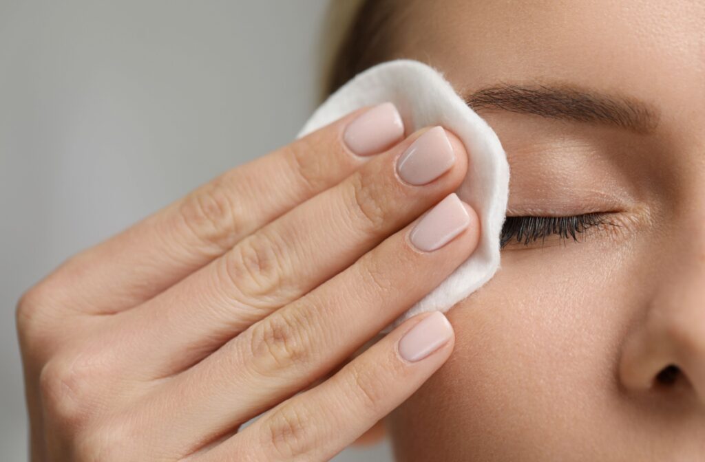 A person is using a white cotton pad to gently wipe makeup off their eyelids.