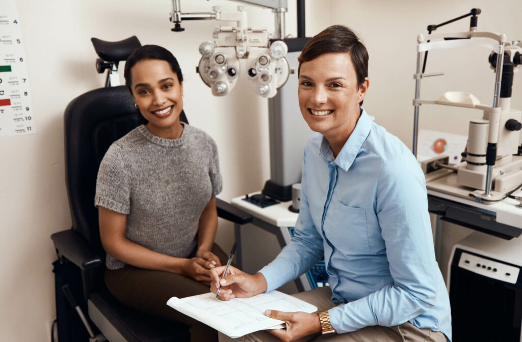 An optometrist and patient smiling at the camera during a discussion about red light therapy in an eye exam.