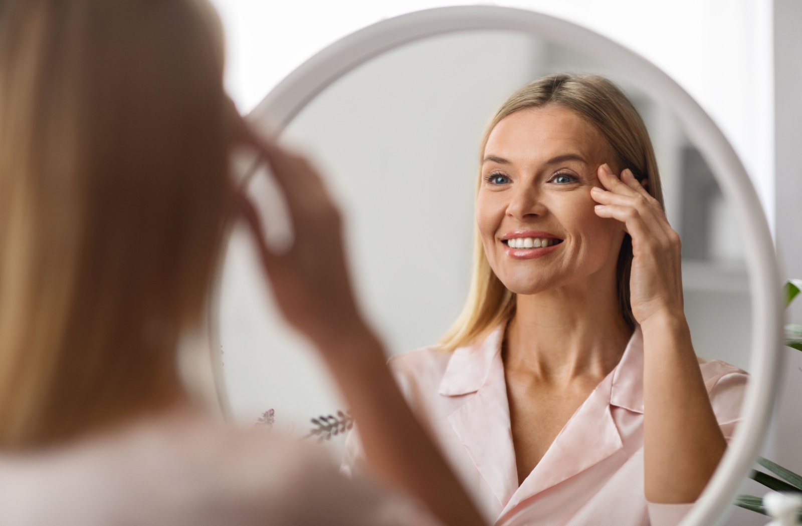 An optometry patient admiring their skin in a mirror after red light therapy treatment.