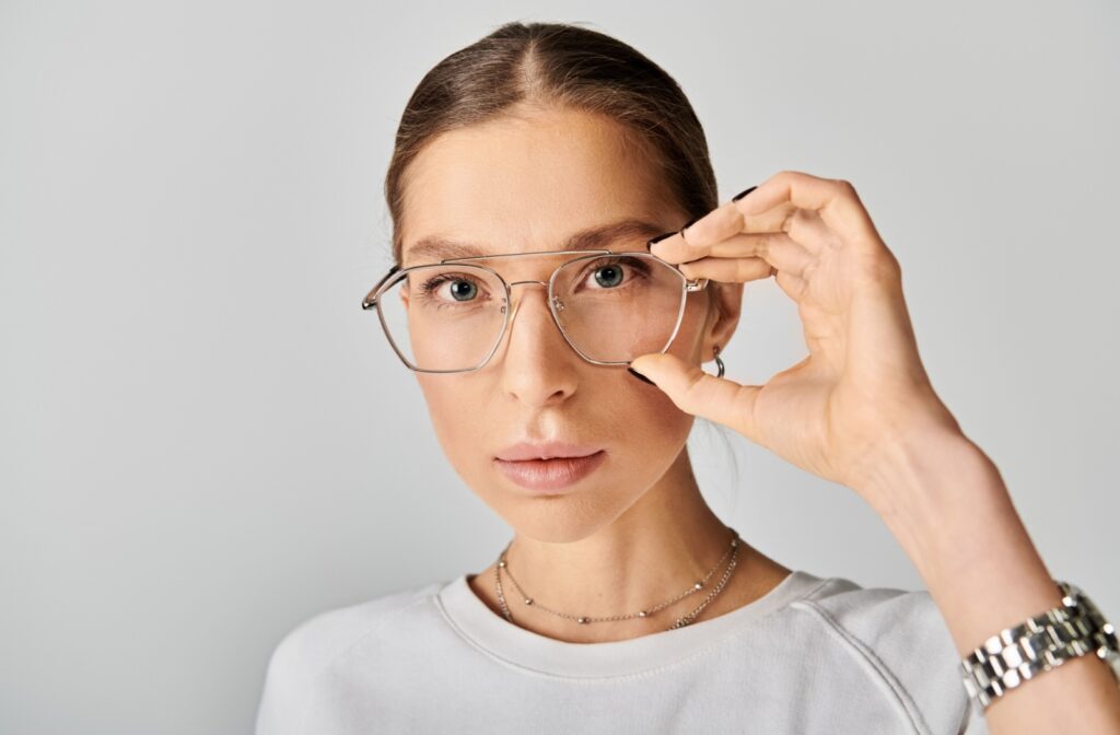 Close-up of a stylish person looking directly into the camera and adjusting their silver, aviator-style glasses