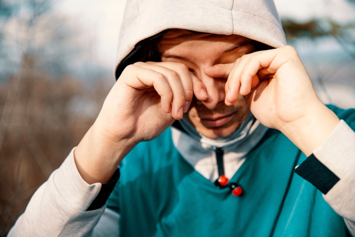 Man wearing hoodie outside rubbing his eyes.